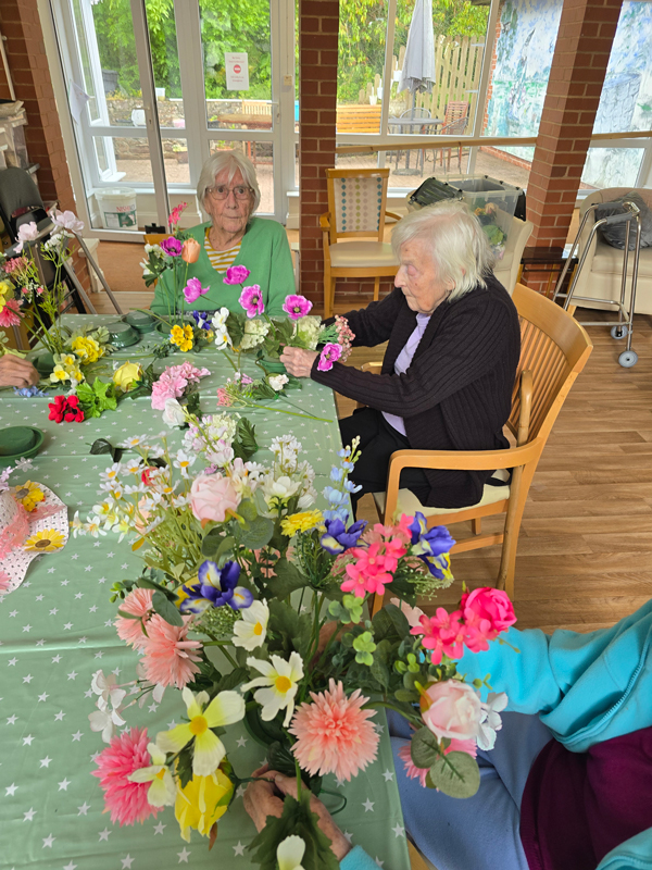 Residents seated together around a table filled with flowers that the residents are placing into arrangements