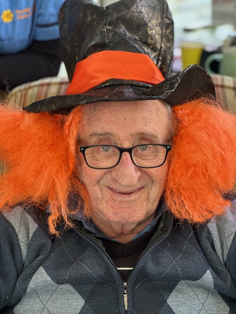 Robin wearing a bright orange wig with a black top hat like the Mad Hatter