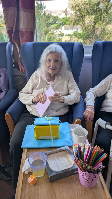 Ruth sitting comfortably in an armchair opening cards and presents