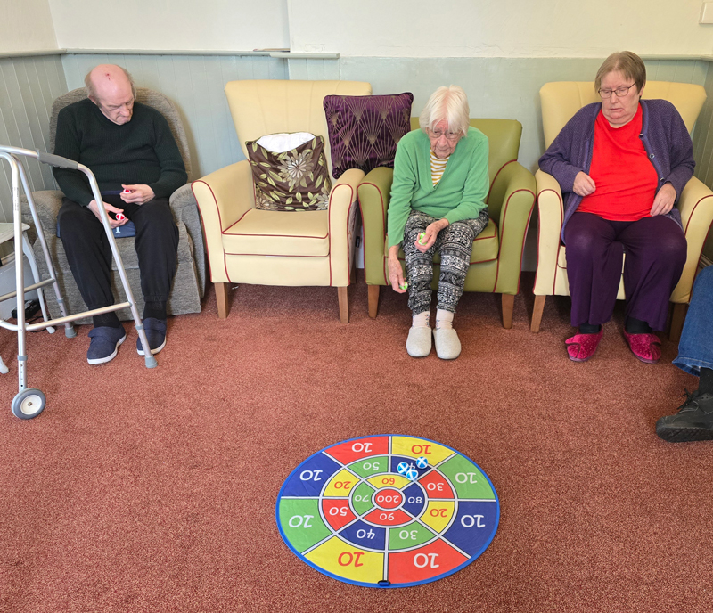Shirley has a go throwing 3 balls on a numbered mat on the floor while team mates watch