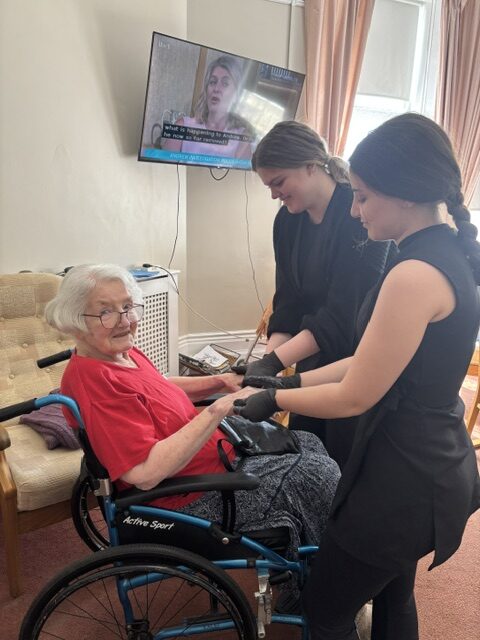 Smiling female resident having both hands massaged by two students rotated