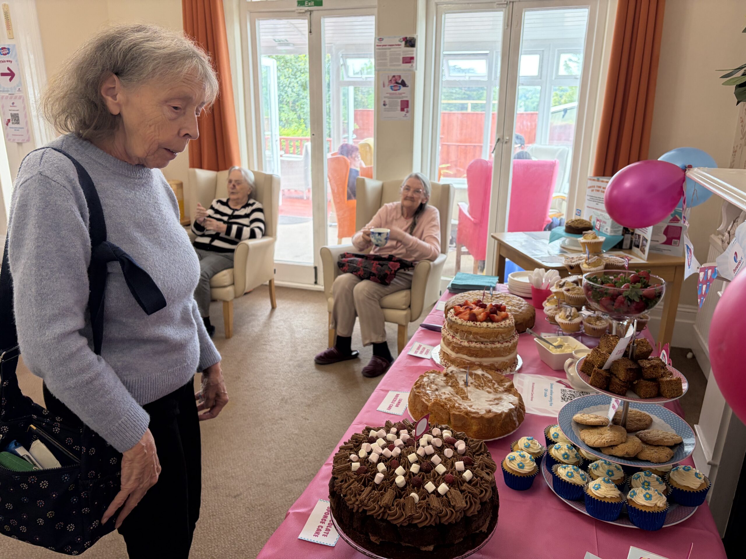 Table laid out with all the cakes for the bake sale and residents seated having a cuppa scaled