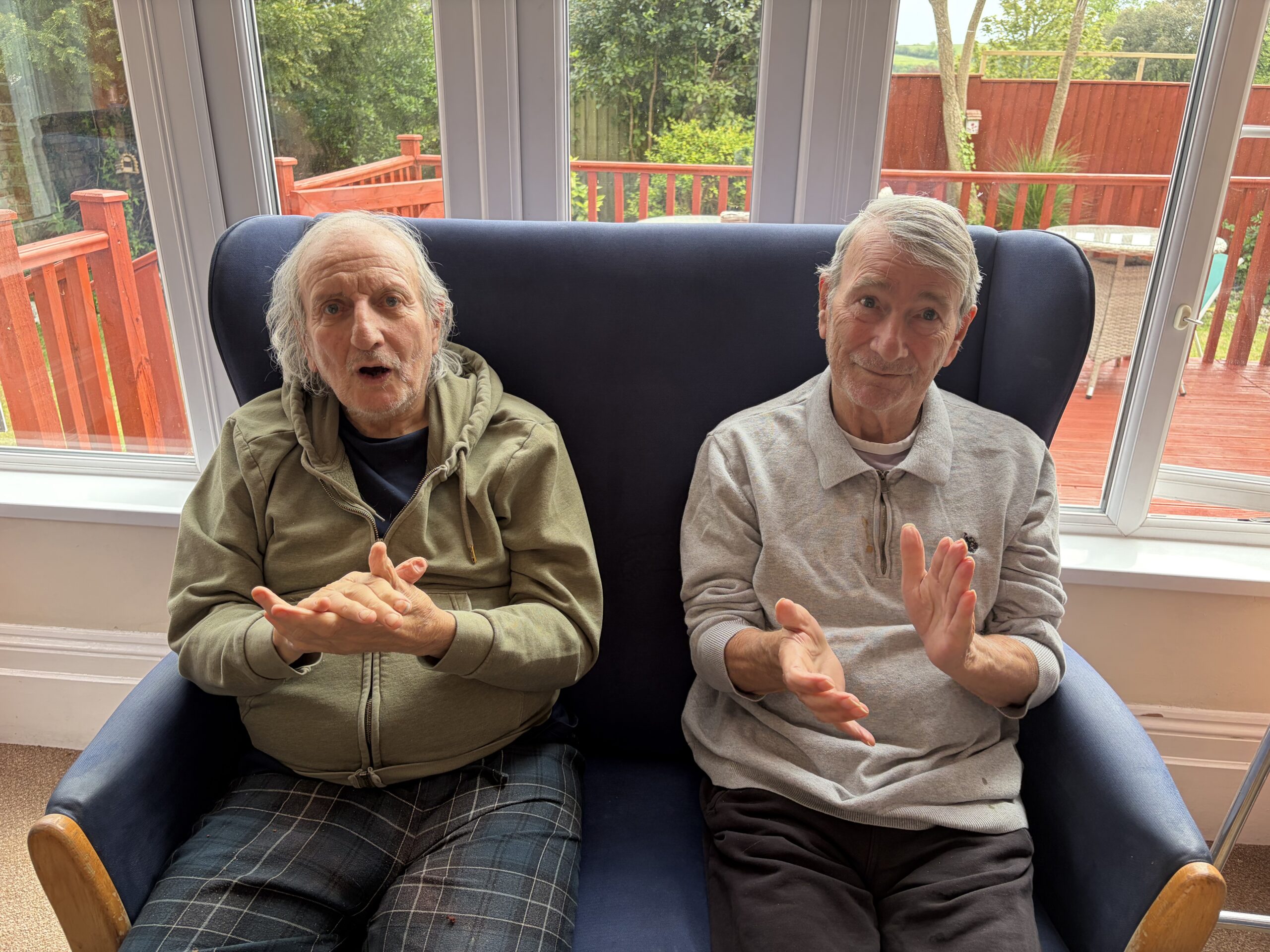 Two male residents seated together clapping to the music scaled