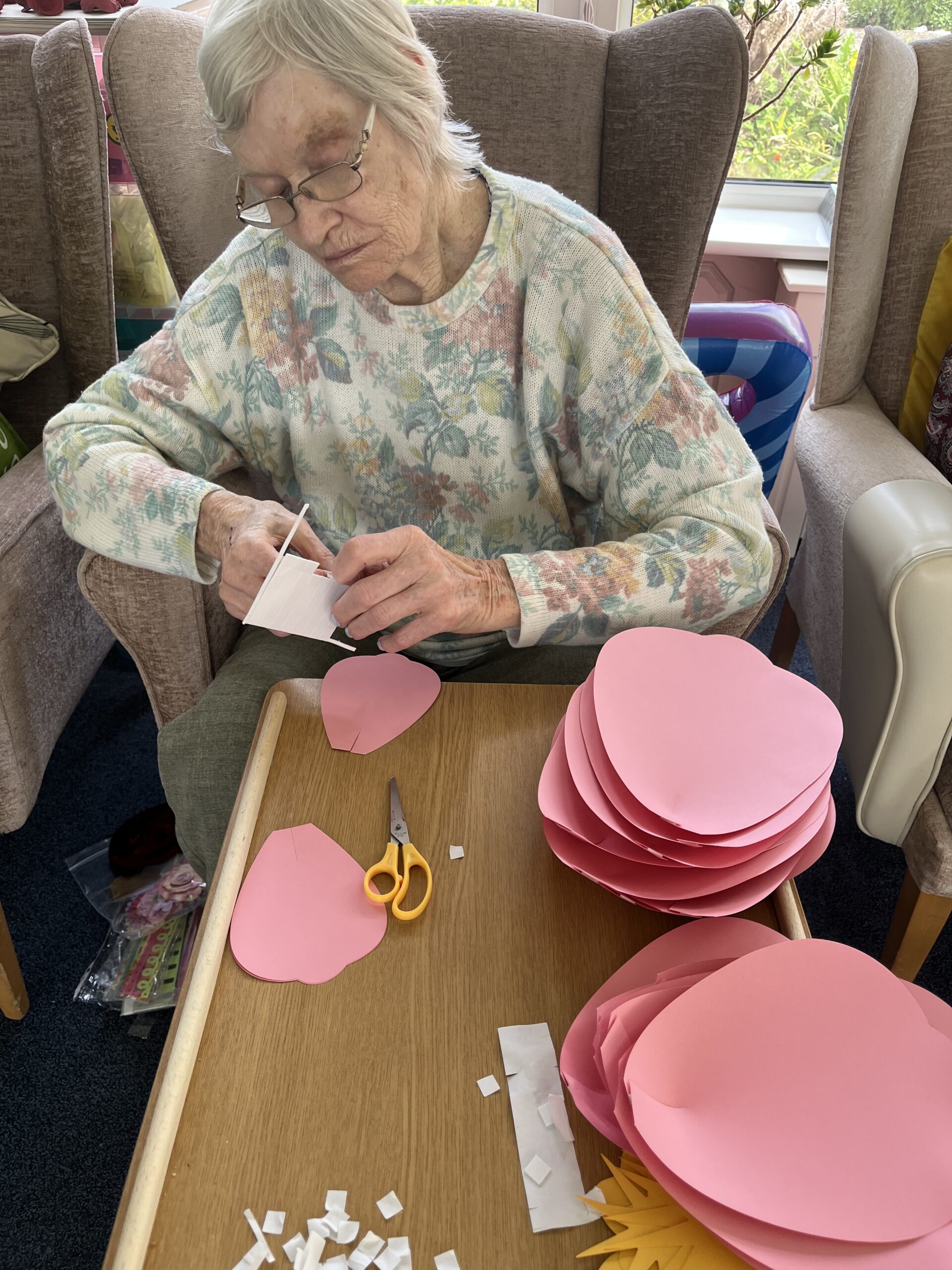 Wendy putting sticky squares on her pink paper flower petals ready for sticking scaled