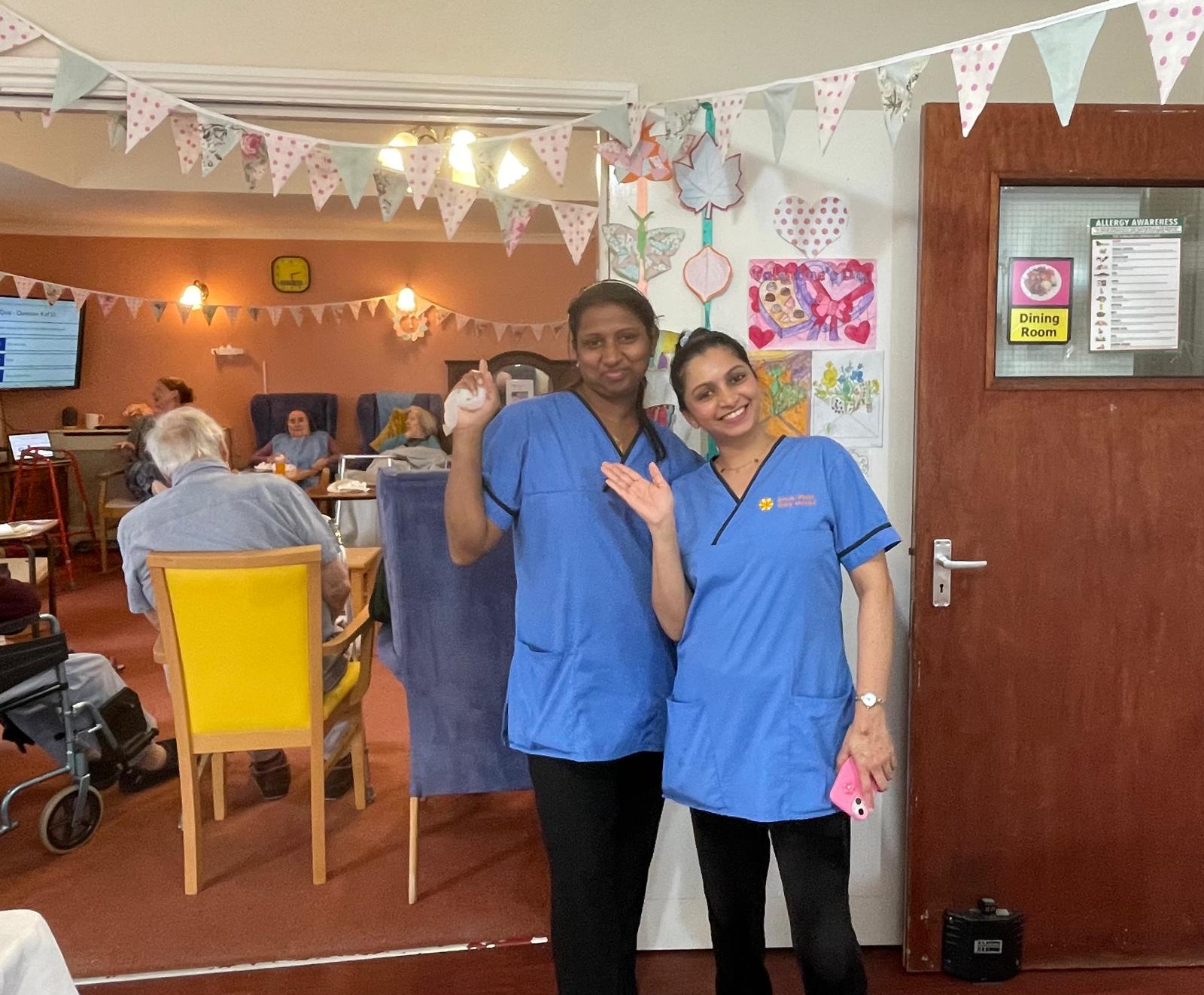 taffcarers posing for a photo pointing at the residents enjoying thrift tea and cake in the background